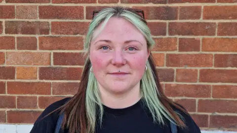 A portrait image of Chelsea, a parent at Firs Primary School. She is stood in front of a brick wall.
