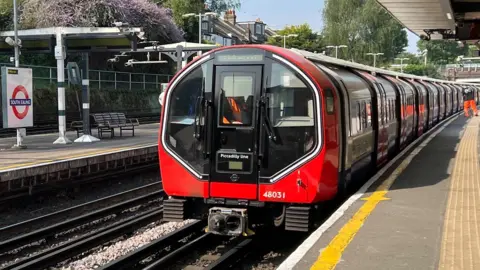 A Tube train with a halo light around the cab is in a station