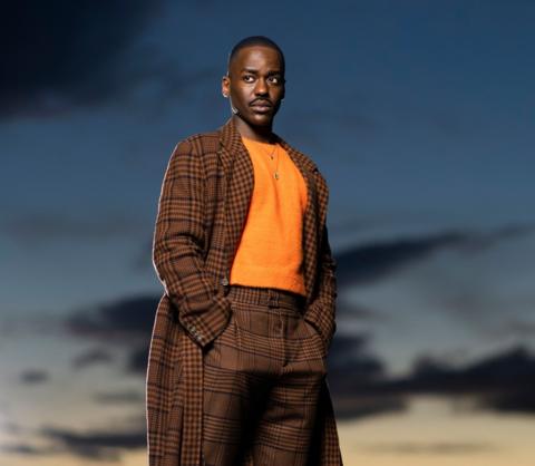 Ncuti Gatwa as The Doctor in a brown suit with an orange jumper