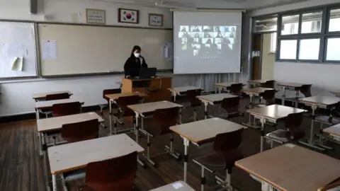 Getty Images Teacher in empty classroom giving online class to pupils via video link