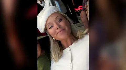 Becky Curtis Selfie of Becky Curtis wearing a white, smart buttoned up blouse and white hat, with many others around her