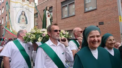 Paul Burnell/BBC Nuns in Green walking with a statue of Our Lady of Revelation brought over from Rome as they walk past new builds in Little Italy, Manchester.