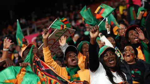 FIFA via Getty Images Fans of Zambia's national football team chant and wave the country's flag