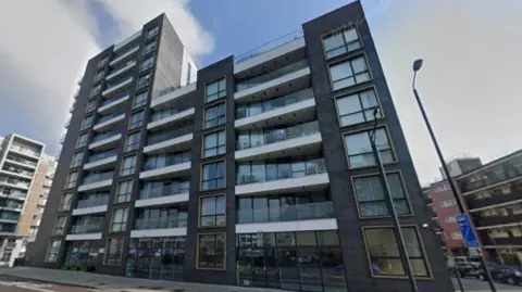 A modern residential block in grey brick with balconies on a London street. 