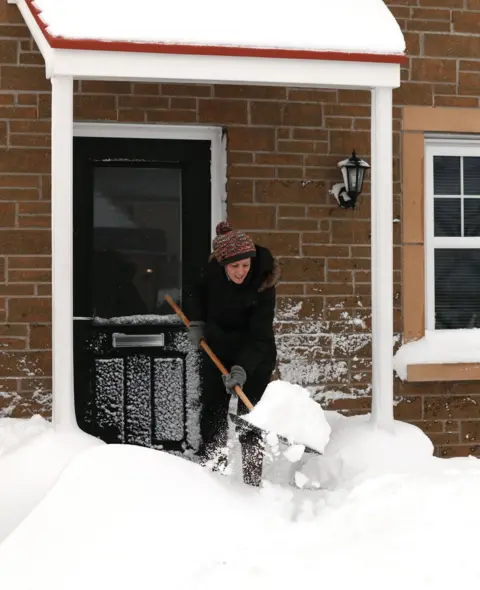 PA A woman clears snow from a doorway