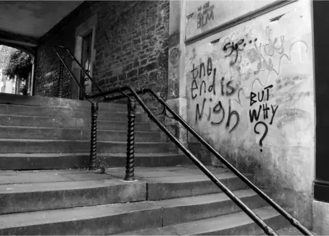 John Bishop Empty Frome street with a stone stairs through a walkway with a wall with graffitti.