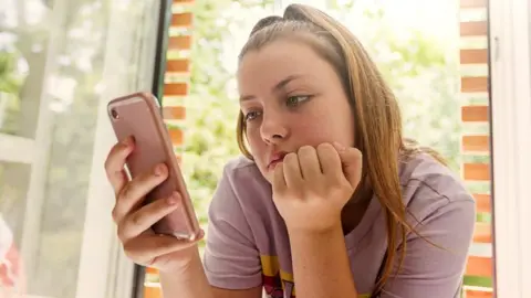 Getty Images Girl looks at phone, sombrely