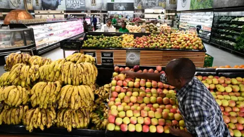Getty Images A shop assistant fills the shelves with fruits and vegetables at a store of Kenyan supermarket chain Naivas in Highridge, Nairobi, on January 18, 2018