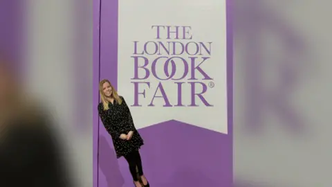 PA Media Chopstick Sally standing in front of a London Book Fair poster