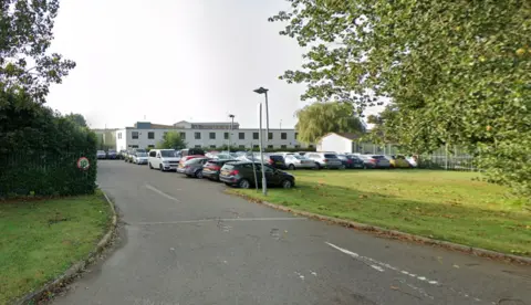 Google Exterior image of HMP Gartree - a white building with parked cars in front of it.