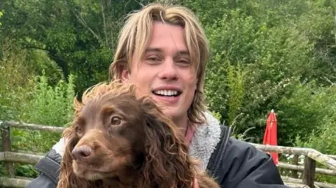 Nicholas Galitzine holding a brown spaniel type dog. 
