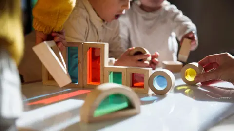 Kids sharing with shapes at a table. You cannot see their faces.