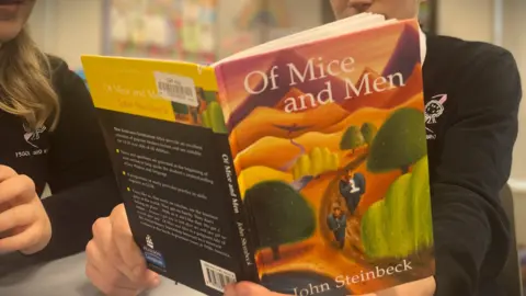 BBC Two pupils in school uniform looking at a copy of the novel Of Mice and Men