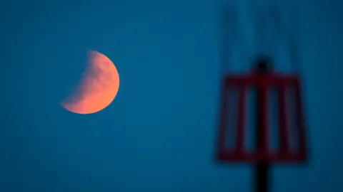 PA Media A picture of the eclipse behind a red tower. The image was taken in Sidmouth.
