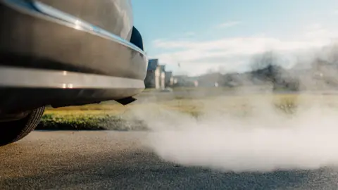 The back of a black car, with exhaust fumes visible.