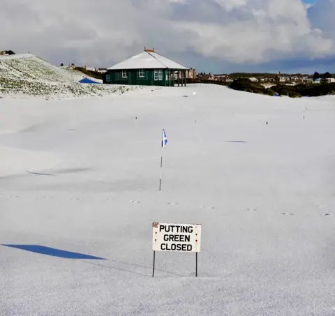 Stewart Paul A golf course with flags covered in snow and a sign saying "putting green closed"