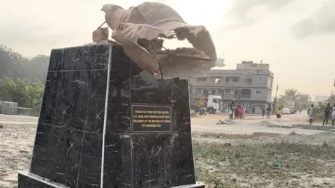 Joseph Amuah A pedestal on which the statue of Nana Akufo-Addo once stood. The words "Thank you from Western Region, H. E. Nana Addo Dankwa Akufo Addo, President of the Republic of Ghana, 6th November 2024" are inscribed on one side of the pedestal, black in colour, and part of the ruined statue on top