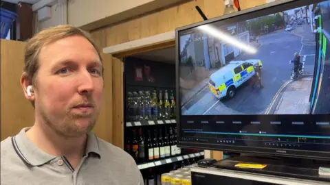 Andrew Turner/BBC Justin Fenn standing next to his CCTV monitor