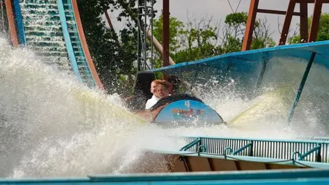 Martin Giles/BBC Two children splash into water while riding a log flume at Pleasurewood Hills.