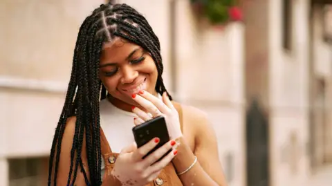 Getty Images Black woman smiles at loving text message from boyfriend on her phone