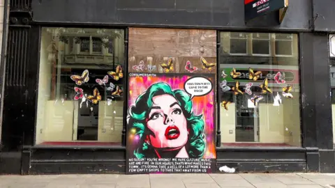 A boarded up shop in Newport with a pop art woman painted onto a board and a speech bubble which reads: "This town has gone to the dogs"