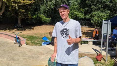 Will Simpson stood with a skateboard, wearing a baseball cap at the new facility in St Margaret's Pastures sports ground