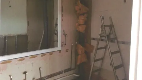 A room mid renovation, showing unplastered walls, a ladder, and visible pipework.