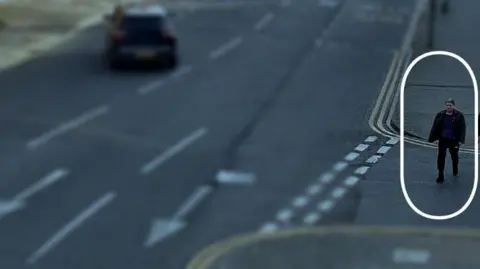 Lincolnshire Police A CCTV image of a man wearing dark clothing walking down a street. The rest of the street is blurred, but the man is circled and his image is clearer than the rest of the photo.