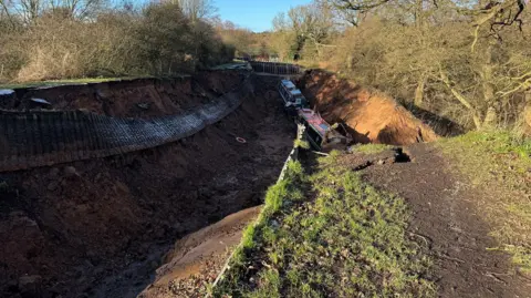 Two canal boats sitting at the bottom of a hole which is empty of water.