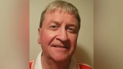 Fergal O'Brien A light-haired man in an orange jersey with a white collar smiles at the camera