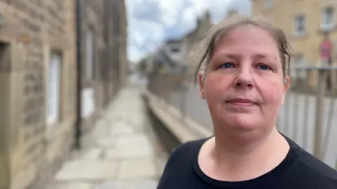Middle-aged Woman in a dark top pictured in front of railings