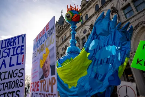 Getty Images Signs against Trump flank a large blue bird that is carried by protestors during a demonstration. 