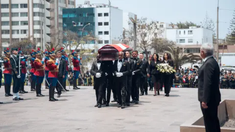 Getty Images Beberapa anggota kongres membawa peti jenazah saat upacara penghormatan terakhir mantan presiden Alberto Fujimori. Peti jenazahnya ditutupi bendera nasional Peru di atasnya dan beberapa anggota keluarganya berjalan mondar-mandir di belakang peti jenazah. Kerumunan dan tentara menyaksikan dari kedua sisi