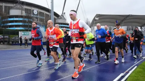 PA Media Sinfield with his head down running past Manchester City's stadium with supporters