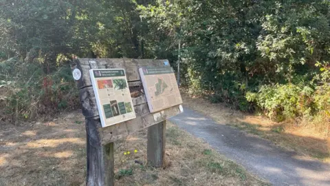 The entrance to a nature reserve, showing a walking path leading into a wooded area
