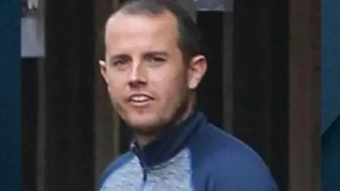 Sean McGovern is seen in a tracksuit top and has short black hair