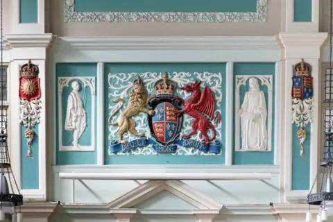 Historic England Ornate plasterwork including a central coat of arms, with white figures either side.