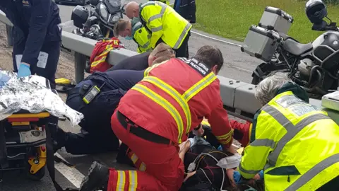 Johan Takats Paramedics crouch around a patient on a roadside