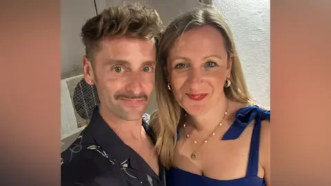 Daniel Harding Daniel and Laura look at the camera. The man has short, dark blond hair and a moustache. The woman has long blonde hair and is wearing a strappy blue dress.