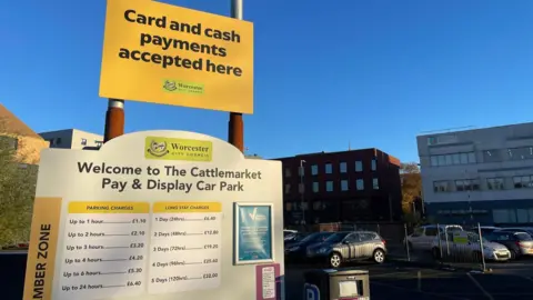 Local Democracy Reporting Service A large sign lists parking charges and timings at Cattlemarket Pay and Display Car Park.