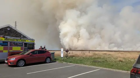 Cat and Fiddle Fire crews in a car park with smoke rising over moorland in the background