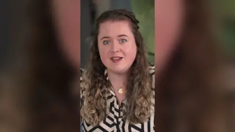 A woman with light brown hair wearing a black and white striped shirt.
