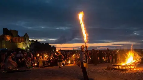 Sue Jones A crowd on Peel Beach as people perform by fire pits
