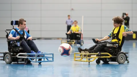 The FA via Getty Images Two players contest the ball during the game. The player on the right, is from Leeds PFC and wears a yellow shirt - the opponent in blue.
