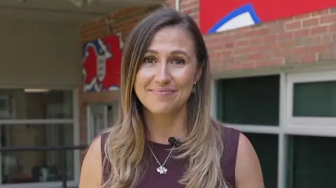 Sarah Dawkins, BBC Sport reporter smiling down the lens wearing a maroon top and silver necklace