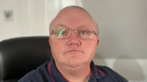 Head and shoulder shot of Warren Archer, wearing silver-framed glasses and a blue polo shirt