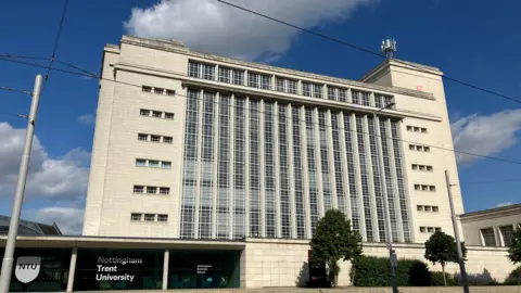 The Newton Building at Nottingham Trent University. It's a tall, pale building with a blue, cloudy sky in the background.