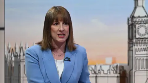 Rachel Reeves wears a pale blue suit jacket and white top on the set of Sunday with Laura Kuenssberg with an illustration of Big Ben behind her 