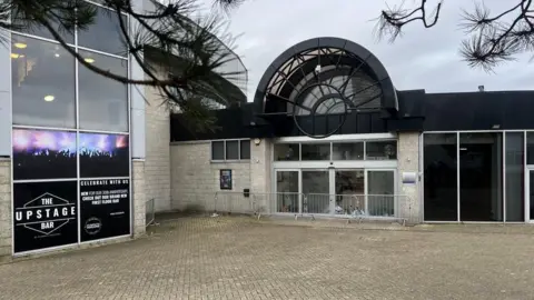 The entrance of the new Plymouth Arena. There are barriers in front of the doors and above it there is a black archway without any sign. 