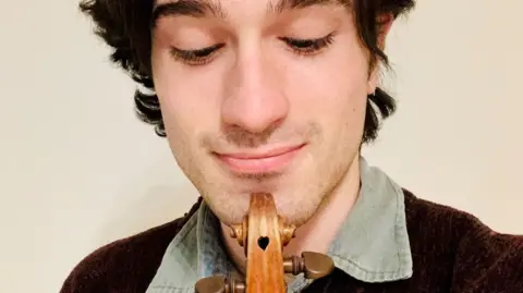 David Lopez Ibanez David Lopez Ibanez holds his violin to his chin as he looks down at it - the instrument has a small heart-shaped hole on top, known as the scroll, of the violin